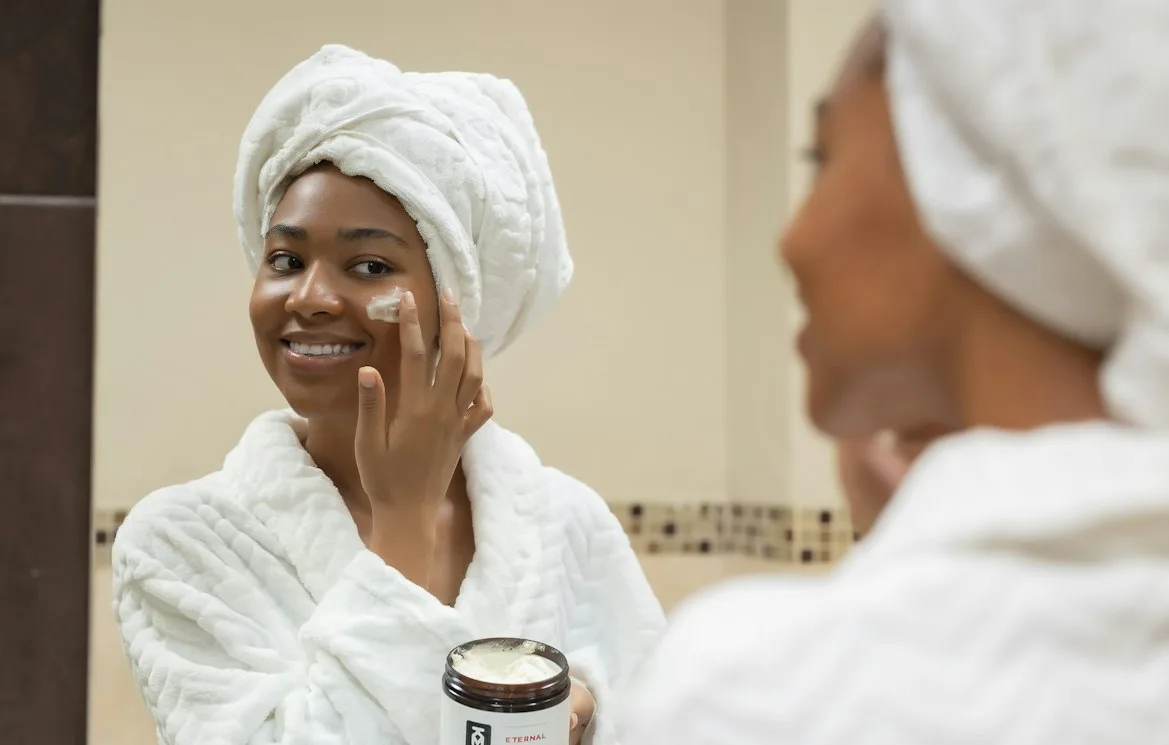 A woman smiling while applying a moisturiser to her cheek